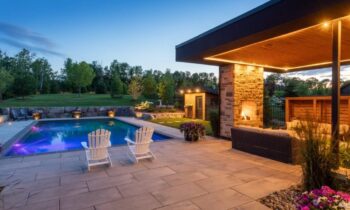 Modern backyard pool with lounge chairs, fireplace patio, and garden lighting at dusk.